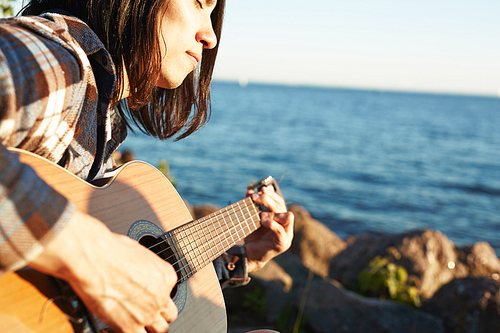 Young man with guitar playing music by seaside on summer day