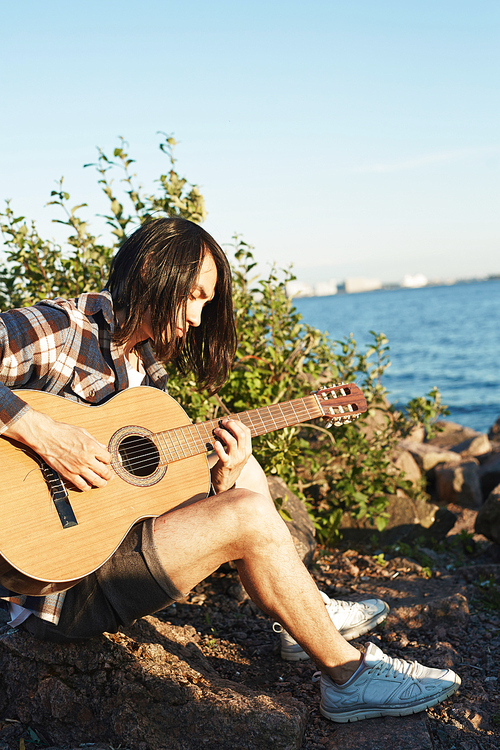 Guy with guitar sitting on beach by water on summer weekend