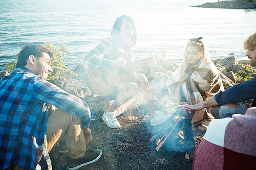 Several happy friends sitting around campfire on summer evening by seaside