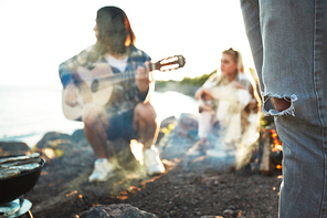 Part of male leg in jeans with two friends having rest by seaside on background