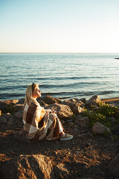 Blonde girl enjoying summer evening by seaside while sitting by water