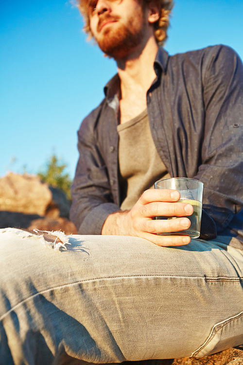 Young man in casualwear holding glass of refreshing drink while relaxing outdoors