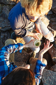 Overview of two young men talking by drink while sitting on stones outdoors