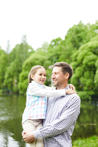 Happy young man holding his little daughter while enjoying summer day by waterside in park