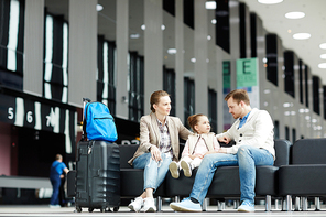 Cute little girl sitting on leather sofa between her parents while waiting for departure announcement