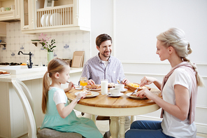 Smiling beautiful family members smiling while eating pancakes and sitting at dining table full of food in cozy kitchen