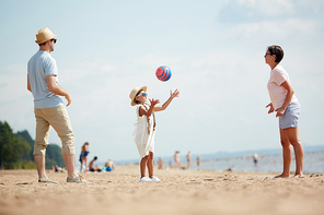 Full length portrait of happy modern family playing ball on beach while enjoying Summer vacation