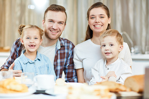 Happy family of four sitting by served table and having breakfast or dinner at home