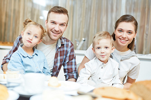 Funny siblings and their young parents  while sitting by table