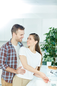 Young man embracing his wife while talking to her in the kitchen by sink