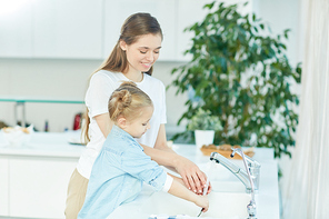 Little girl helping her mother wash dishes in the sink in the kitchen