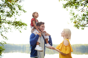 Young restful family of three enjoying summer weekend by waterside in the country