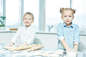 Little adorable siblings standing by table while preparing homemade pastry