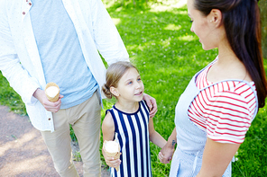 Cute girl with icecream talking to her mother while taking walk with parents on summer day