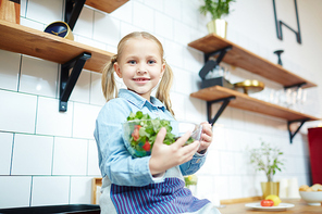 Smiling little girl with bowl of fresh vegetable salad  in the kitchen