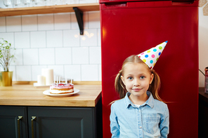 Cute child in birthday cap  in the kitchen with homemade cake on background