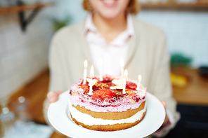 Yummy homemade birthday cake with burning candles held by female