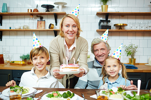 Grandparents and grandchildren in birthday caps celebrating holiday at home