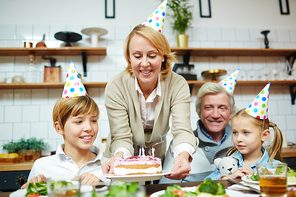 Happy woman putting birthday cake on festive table for her family