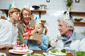 Little girl opening gift-box with birthday present and expressing amazement during home celebration