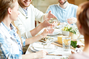 Young man pouring homemade lemonade in glass of his girlfriend while having dinner with friends