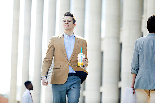 young businessman in formalwear carrying drink while moving in urban