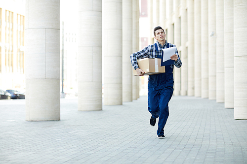 Young courier running along column rows while delivering package to one of clients in business center