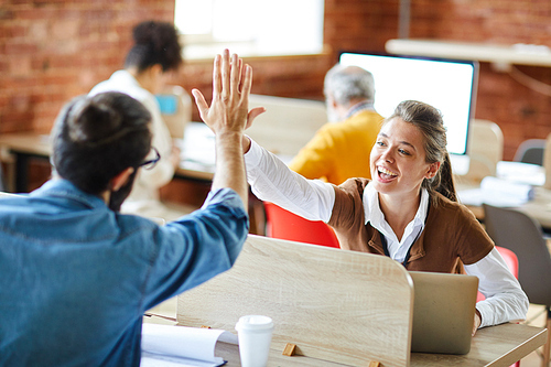 Cheerful and successful businesswoman giving high five to her colleague sitting in front of her
