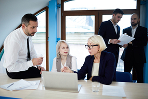 Two co-workers listening to mature trader or analyst explaining them online data at meeting