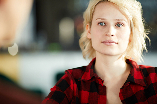 Head and shoulders portrait of creative  young woman wearing casual shirt listening to colleague during meeting and smiling, copy space