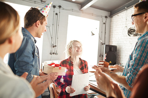 Portrait of creative young people celebrating Birthday in office, focus on happy blonde woman receiving cake and gifts, copy space