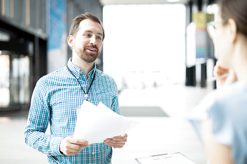 Young economist with papers having talk with his client or colleague at meeting in lounge