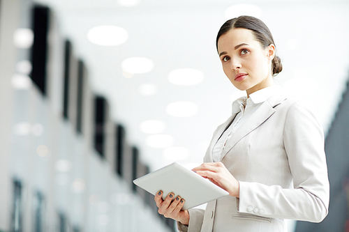 Confident young businesswoman with tablet looking straight while networking and thinking of ideas in airport lounge