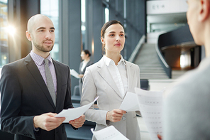 Two young delegates with papers talking to their foreign colleague before business or political conference