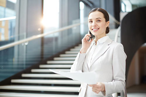 Young professional in elegant suit standing by staircase in airport and consulting client about terms of contract