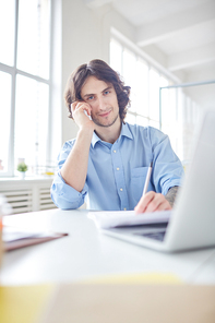 Portrait of businessman having a conversation on the phone and making notes at the table