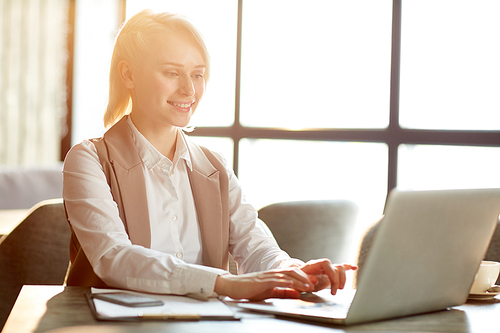 Young manager sitting in cafe in front of laptop and searching for necessary information in the net