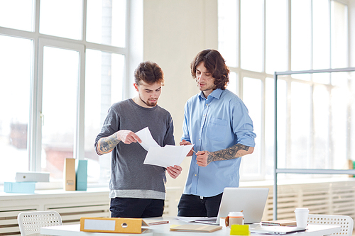 Two coworkers in a modern office in discussion over documents