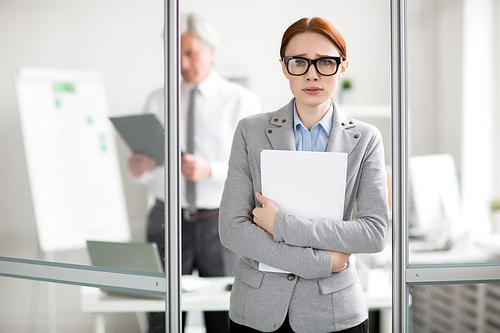 Scared employee with documents standing by door of her boss office and going to talk to him