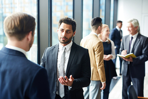 Confident handsome mixed race businessman with beard sharing his opinion with forum participants and gesturing hands during conference break