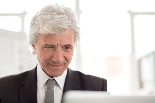 Mature wrinkled businessman with grey hair working with online information in office