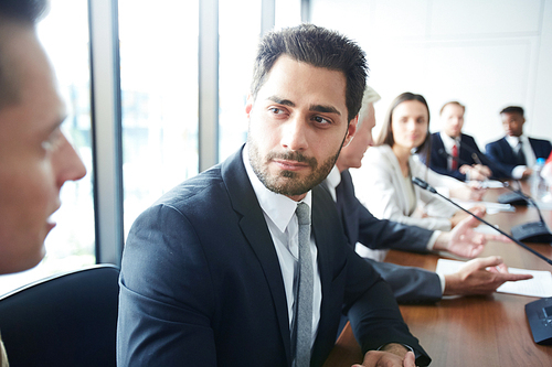 Head and shoulders portrait of handsome businessman looking at colleague while sitting at meeting table in conference room, copy space