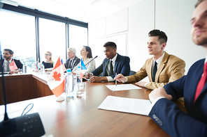 Confident interracial representatives of Commonwealth countries sitting at conference table and listening to rapporteur at meeting