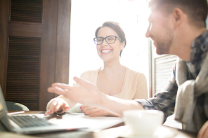 Attractive man and woman smiling and consulting about new project while sitting at cafe table near laptop.