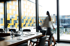 Background image of conference room in modern office with blurred shape of businesswoman crossing it, copy space