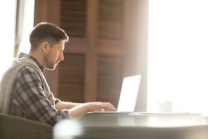 Side view of businessman in casual outfit sitting at cafe table and using laptop.