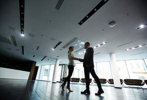 Low angle view of confident entrepreneur greeting his female business partner with firm handshake while standing at spacious office lobby