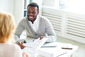 Happy young businessman pointing at contract while explaining its terms to partner during negotiation