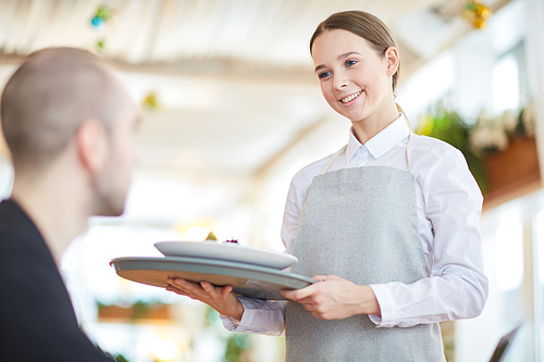 Young waitress with tray bringing order of her client in restaurant