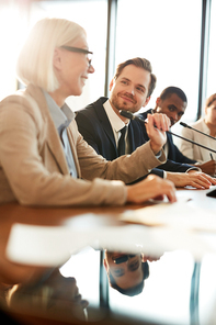 Young confident delegate listening to mature colleague speaking in microphone at conference